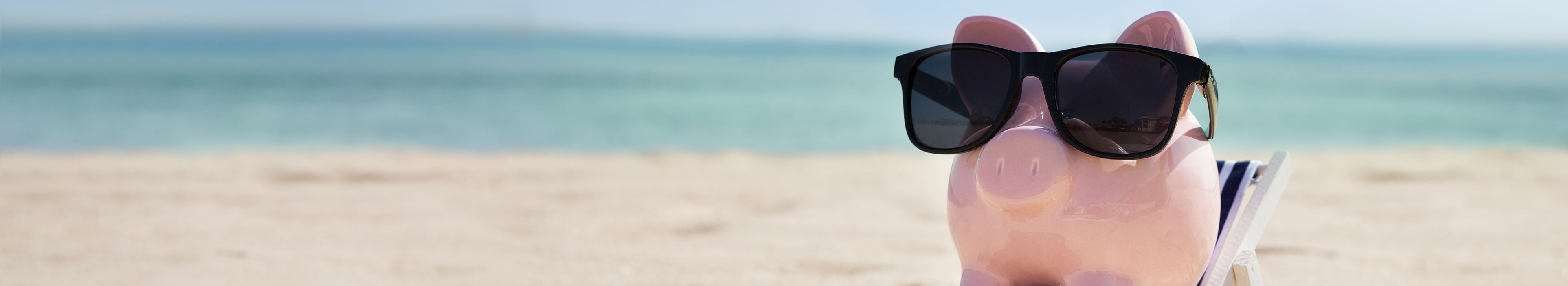 Sparschwein mit einer Sonnenbrille liegt auf einer Liege am Strand