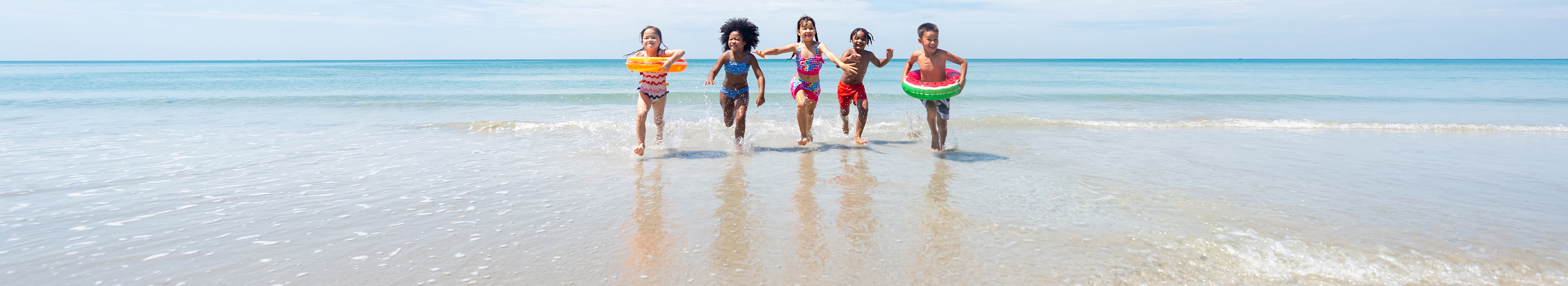 Fünf Kinder rennen am Strand aus dem Wasser