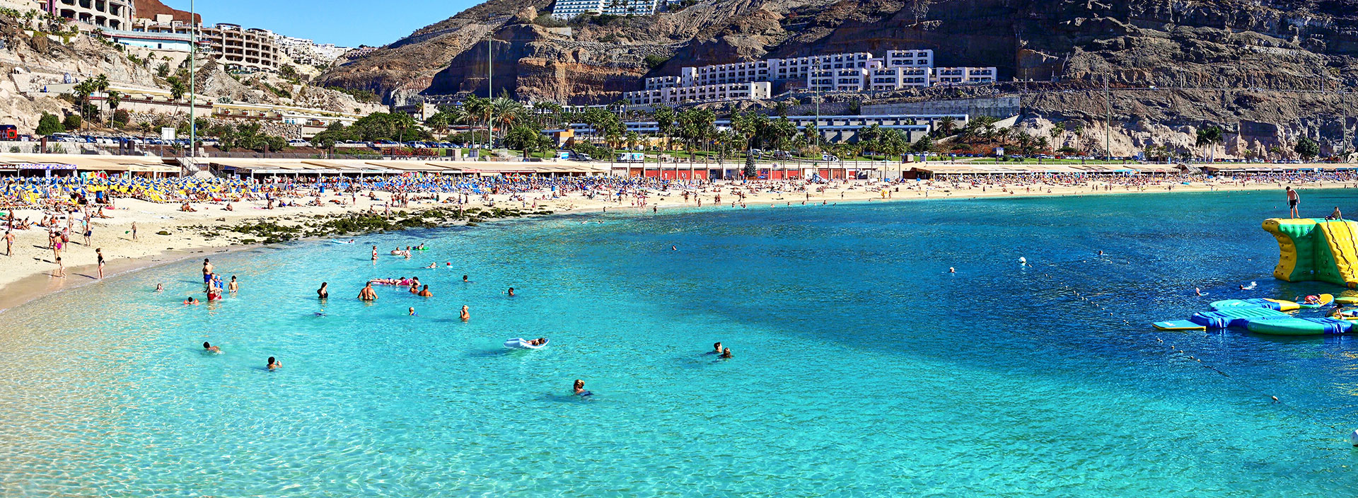 Ein Sandstrand auf Gran Canaria an einem sonnigen Tag mit vielen Badegästen.