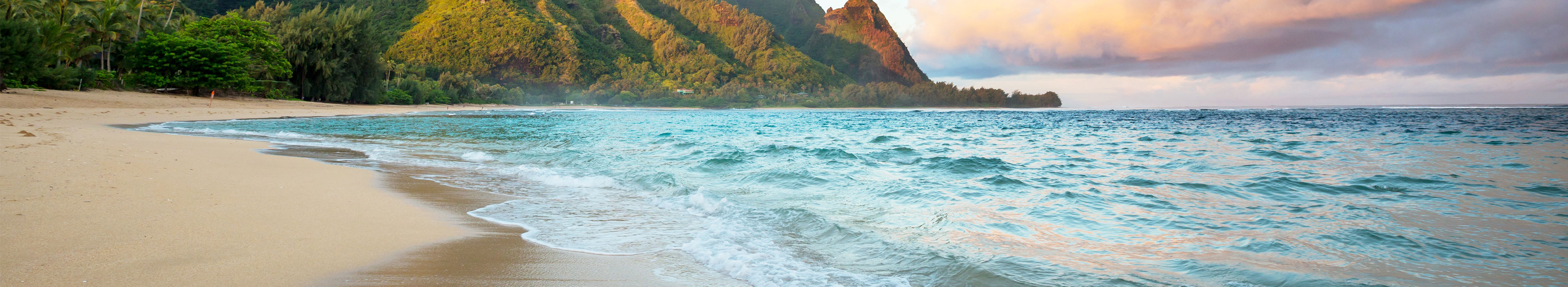 Wunderschöner Strand auf Hawaii, im Vordergrund das Meer und Sand, im Hintergrund Berge.