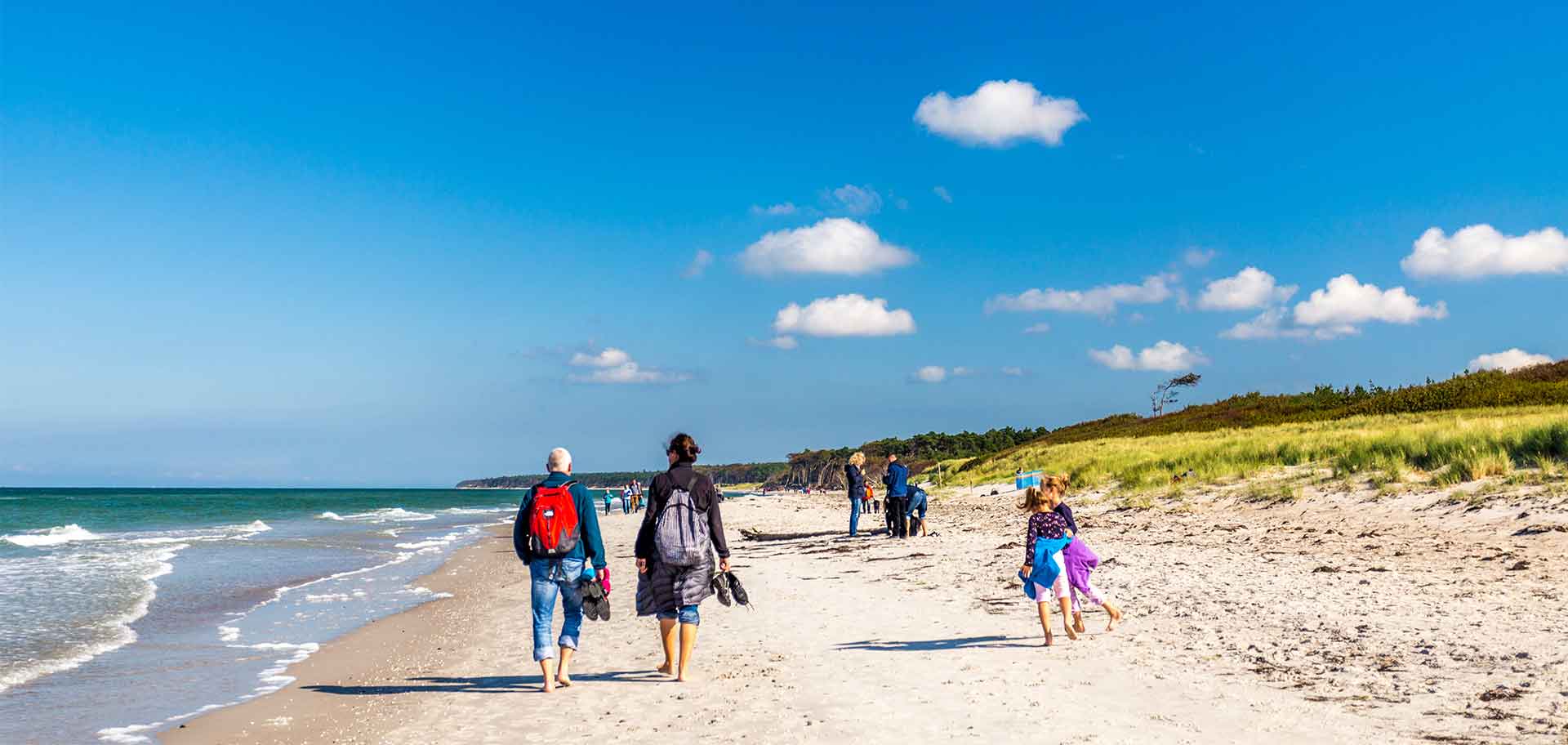 Eine Familie mit Kindern läuft am Strand an der Ostsee entlang.