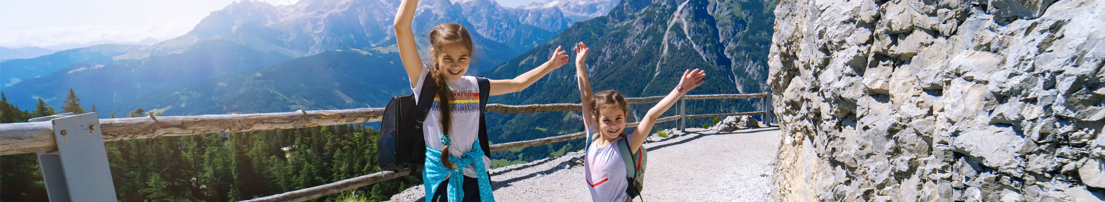 Kinder wandern an einem schönen Sommertag in den österreichischen Alpen, ruhen sich auf einem Felsen aus und bewundern die herrliche Aussicht auf die Berggipfel.
