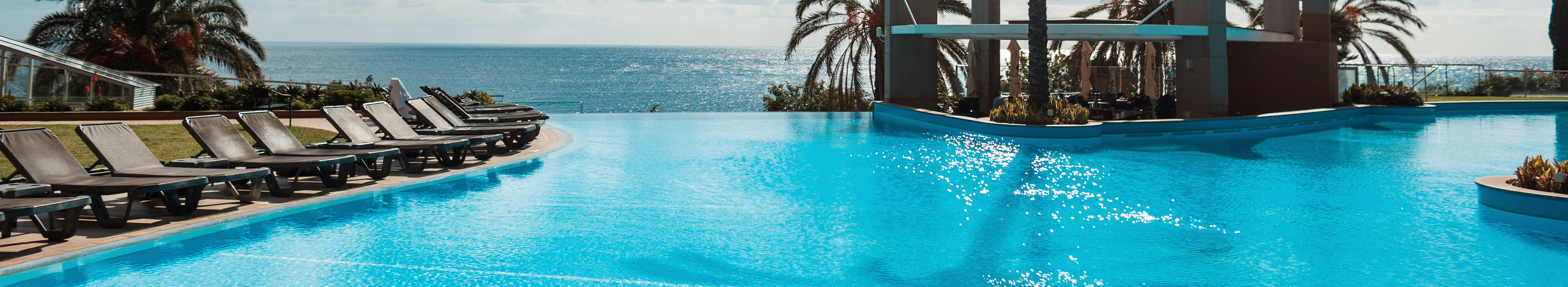 Hotel auf Madeira, Pool und Blick auf das Meer. Am Rand Liegestühle und Palmen.