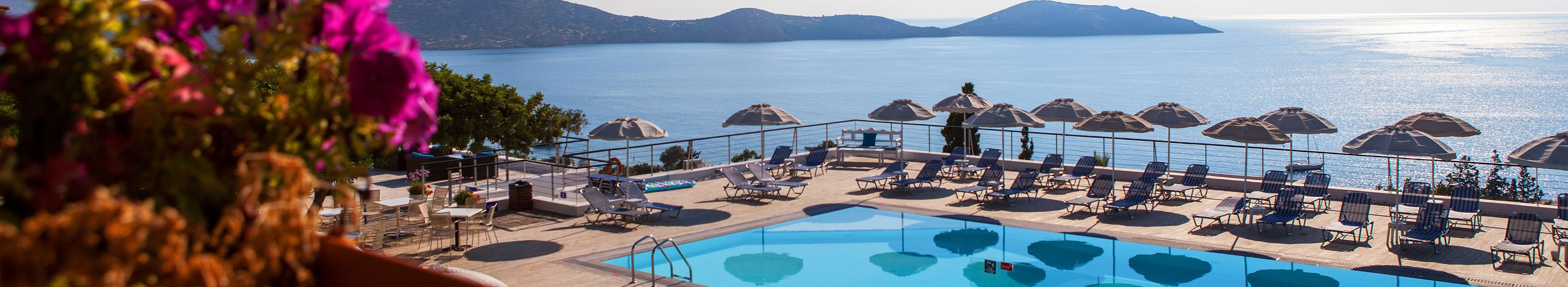 Hotel auf Kreta, Pool mit Liegen und Sonnenschirmen, im Hintergrund das Meer. 