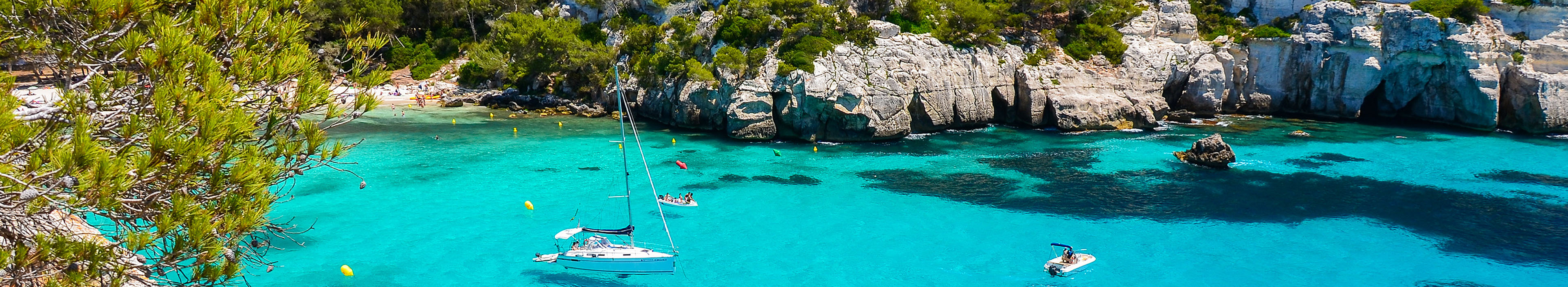 Aussicht auf türkisblaues Wasser und weiße Boote am Strand von Cala Macarelleta, Menorca.