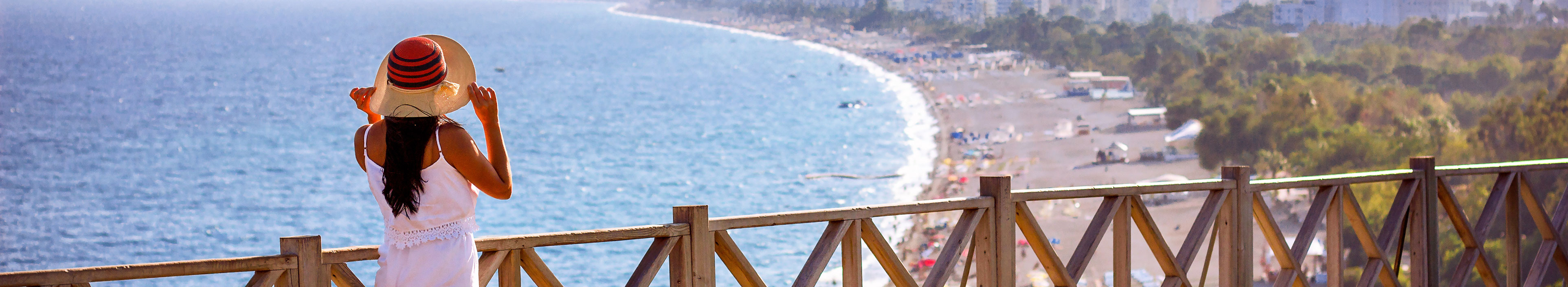 Eine Frau blickt auf das Meer der Türkei, im Hintergrund sind Berge zu sehen.