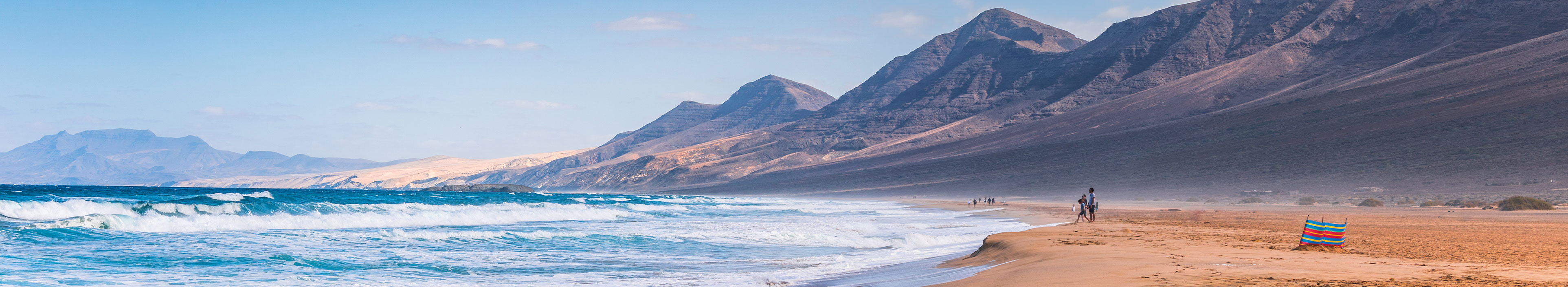 Urlaub Gran Canaria. Meer mit hohen Wellen und Menschen die am langen weitläufigen Strand laufen.