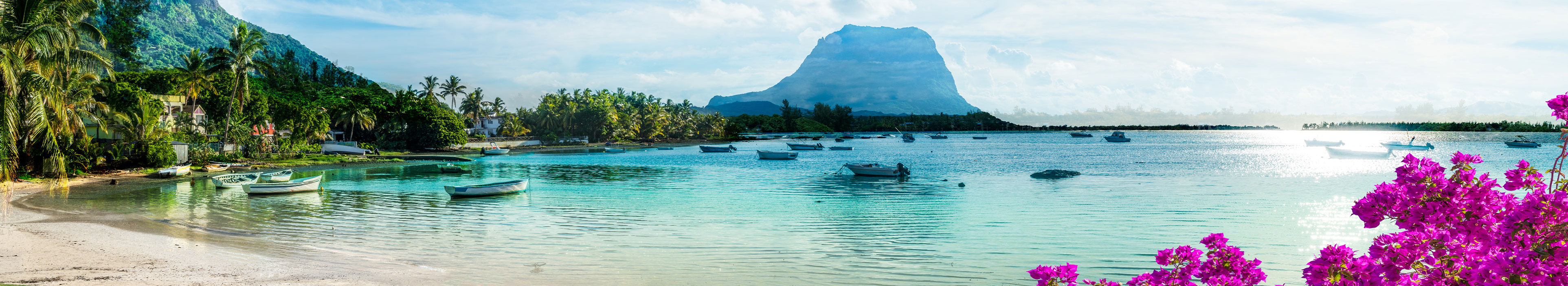 Urlaub Mauritius. Viele kleine Fischerboote auf dem Meer, im Hintergrund grüne Landschaft und Berge. 