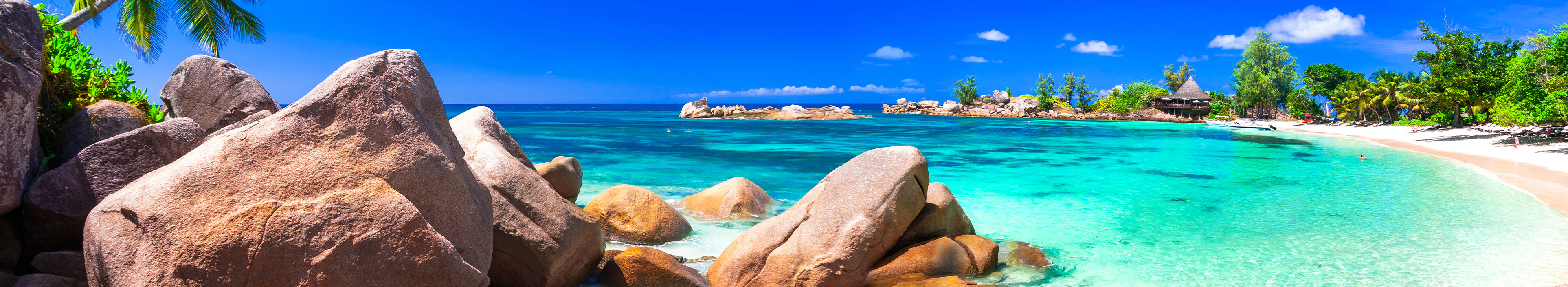 Urlaub Seychellen. Weißer Strandabschnitt mit türkisblauem Meer und im Hintergrund grüne Bäume.