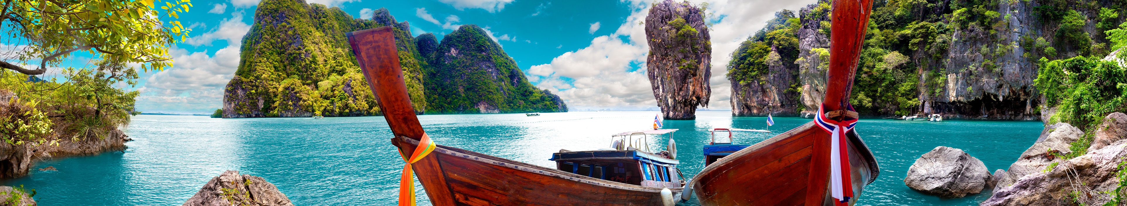 Urlaub Thailand. Zwei rote Holzboote auf türkisblauem Wasser und im Hintergrund Felsen.