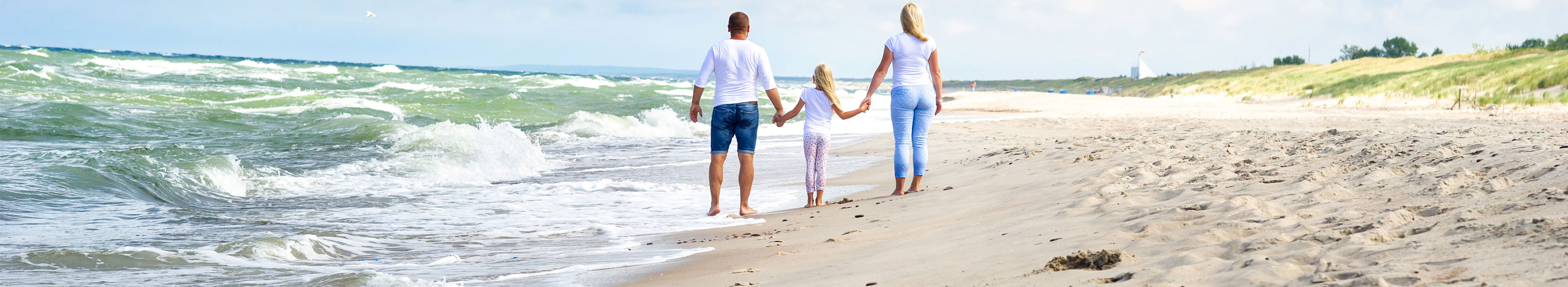 Ein kleines Mädchen und seine Eltern spazieren am Strand der Ostsee